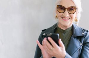 Starsza kobieta w okularach trzyma telefon w dłoni